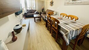 A living room with a sofa, a coffee table, a dining table with chairs, a TV mounted on the wall, and a painting on the wall. - A1018 - Comfort and tranquility by the sea (Cala de Finestrat)