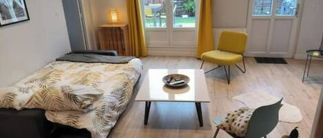A bedroom with a bed, a small table, a chair, and a window with curtains.