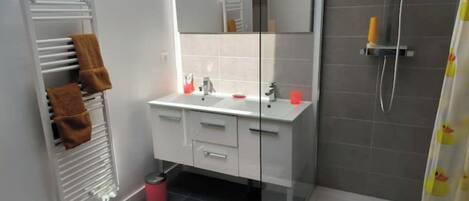 Et moderne badeværelse med brusekabine i glas, et hvidt toiletbord med spejl og et håndklædestativ med brune håndklæder.