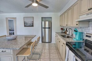 A modern kitchen with a stainless steel refrigerator, granite countertops, and a ceiling fan.