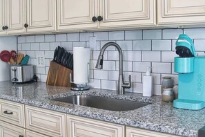 A kitchen with a granite countertop, stainless steel sink, and a teal coffee maker. - Fillmore Unit #8 | 2BR/1BA (Cape Canaveral)