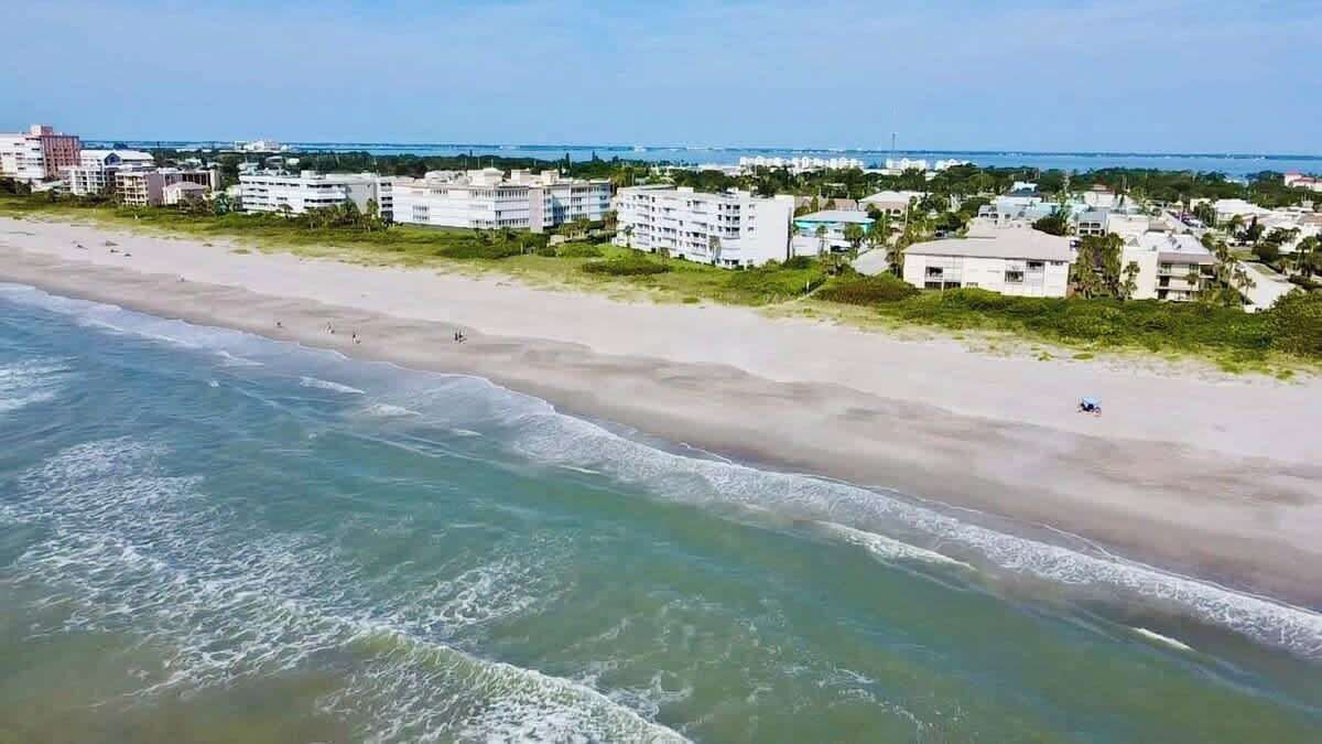 A beach with a clear view of the ocean and a row of buildings in the background.