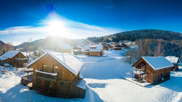 Un pueblo cubierto de nieve con cabañas de madera, cielo despejado y una montaña al fondo.