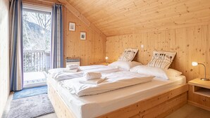 Un dormitorio de cabaña de madera con dos camas, una ventana con cortinas, una mesita de noche con una lámpara y un cuadro en la pared.