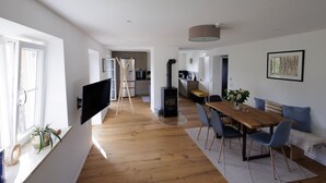 A modern living space with a wooden dining table, blue chairs, a TV mounted on the wall, a kitchen area, and a large window. - Alpenchalet Bad Reichenhall, flat for 2-4 pax, luxury interior, fantastic view (Bayerisch Gmain)