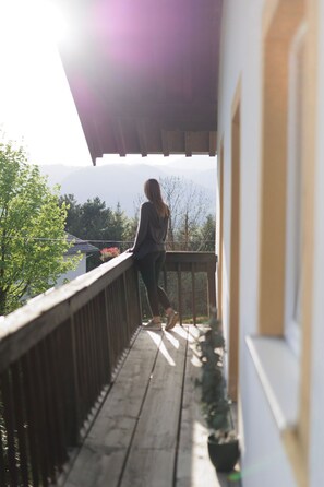 A person standing on a wooden deck with a view of mountains and trees.