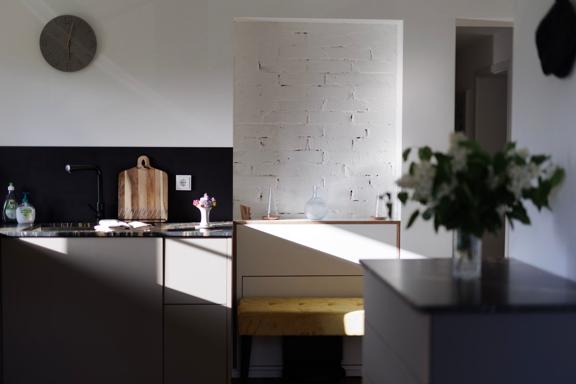 Eine moderne Küche mit Backsteinwand, Schneidebrett aus Holz und einer Vase mit Blumen auf der Arbeitsfläche.