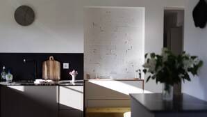 A modern kitchen with a brick wall, a wooden cutting board, and a vase with flowers on the counter. - Alpenchalet Bad Reichenhall, flat for 2-4 pax, luxury interior, fantastic view (Bayerisch Gmain)