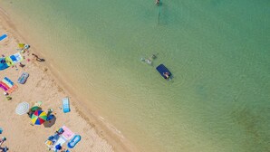 An aerial view of a beach with clear water, people swimming, and beachgoers relaxing under umbrellas. - Villa Katarina Privlaka (Privlaka)