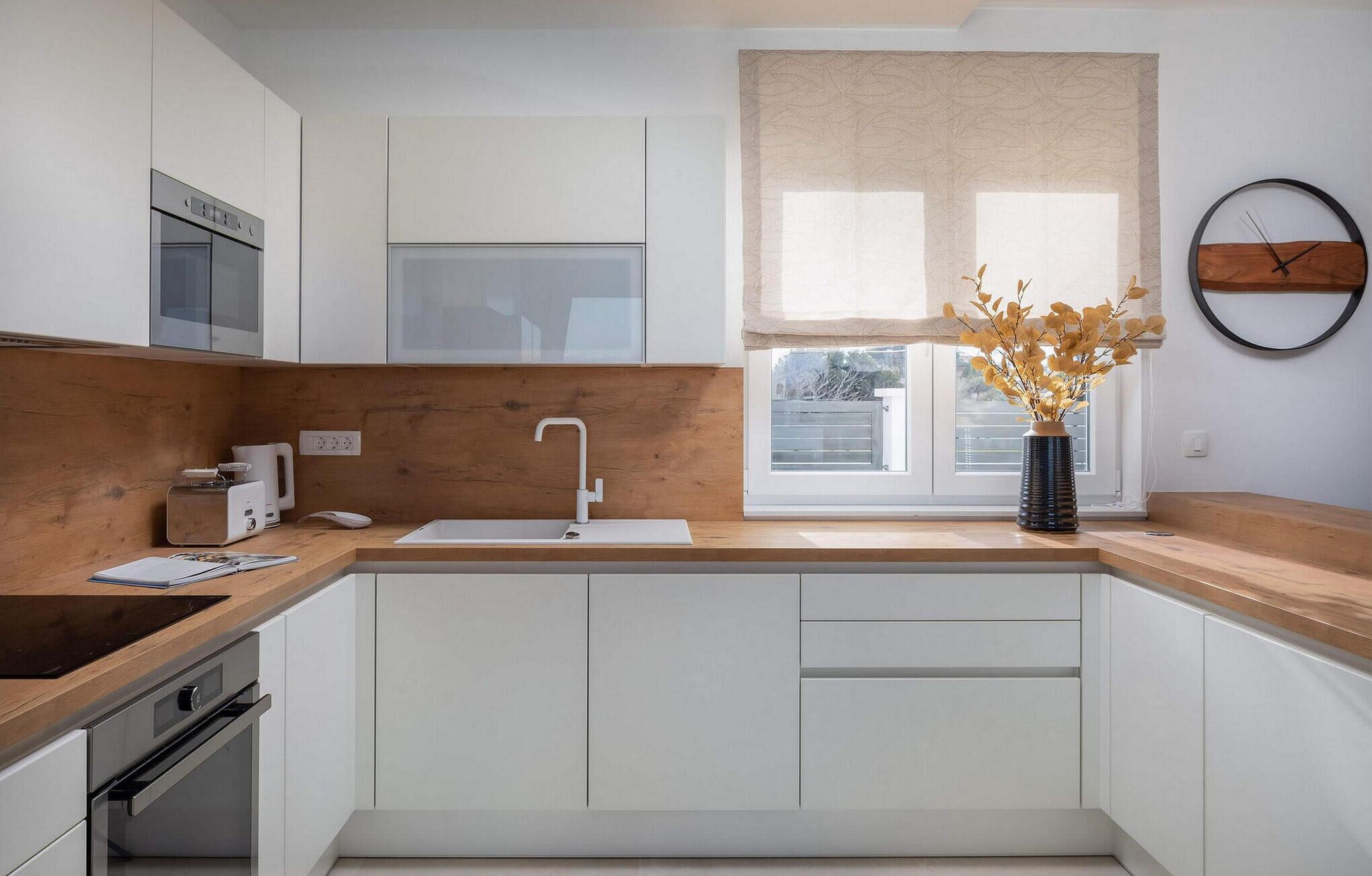 Een moderne keuken met witte kasten, een houten aanrecht, een inbouwoven, een spoelbak en een raam met uitzicht.