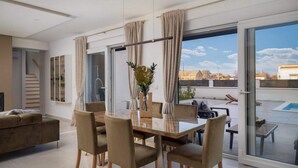 A modern living room with a glass dining table, comfortable seating, and a view of a swimming pool and buildings. - Villa Katarina Privlaka (Privlaka)