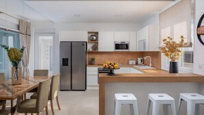 A modern kitchen with a central island, stainless steel appliances, and a dining area with a glass table and chairs. - Villa Katarina Privlaka (Privlaka)