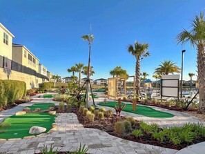 A golf course with a brick pathway, palm trees, and a clear blue sky.
