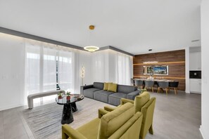 Ein modernes Wohnzimmer mit einem grauen Sofa, gelben Sesseln, einem runden Couchtisch und einem Essbereich mit weißem Tisch und Stühlen.