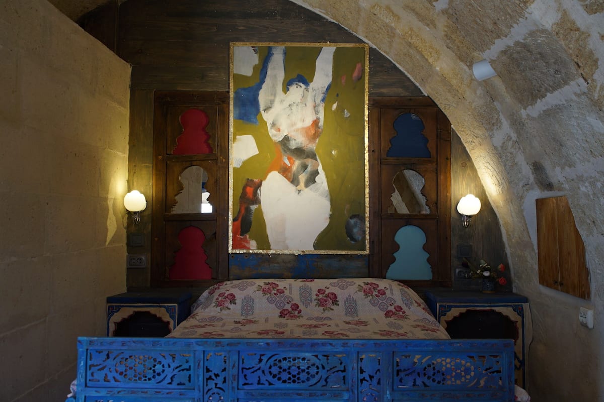 Une chambre à coucher avec un lit, un grand tableau abstrait et deux lampes fixées au mur.