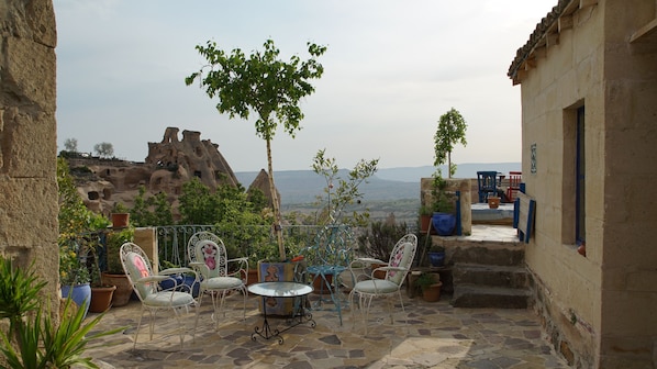 An outdoor patio with stone flooring, metal chairs, and tables, surrounded by potted plants and a view of a mountainous landscape. - Dancing Cloud Art Pansion (Nevsehir)