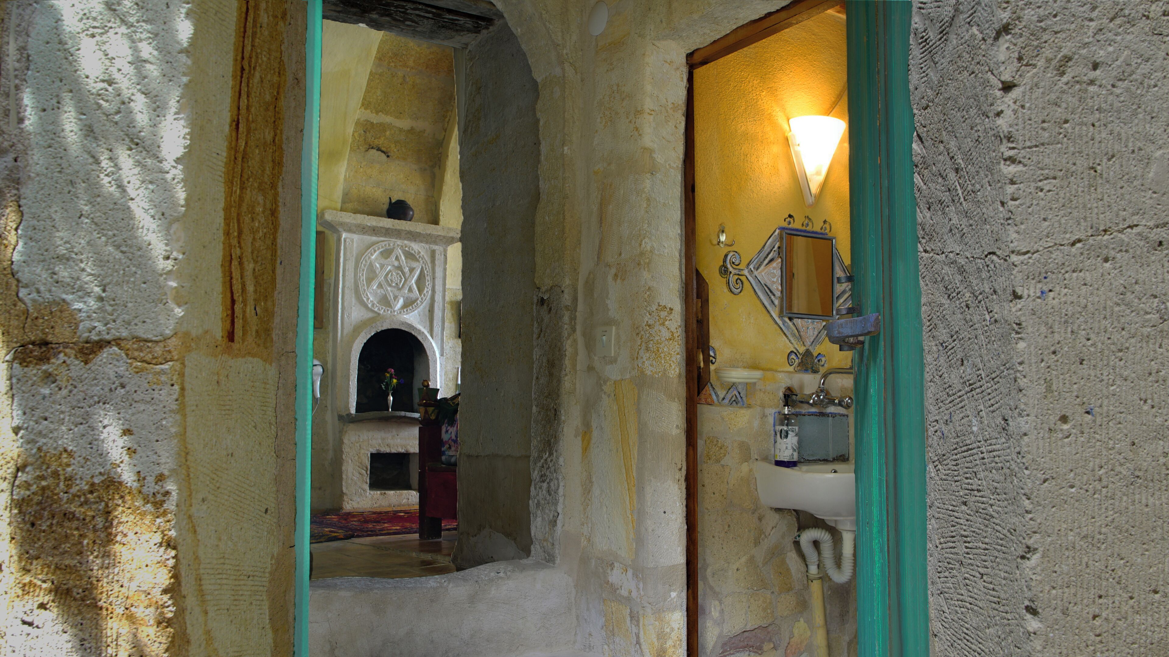 A narrow hallway with a stone wall, a small alcove with a decorative arch, and a bathroom with a sink and mirror.