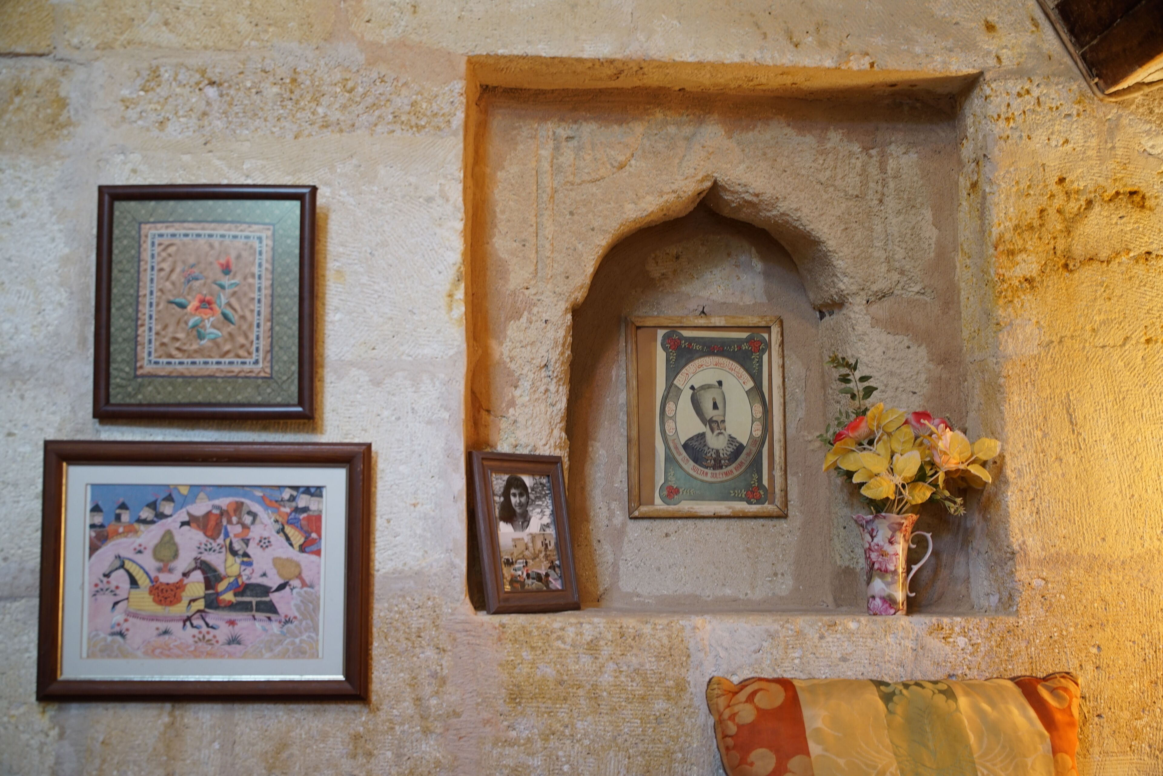A wall with framed artwork, a small alcove with a framed portrait, and a vase with flowers.