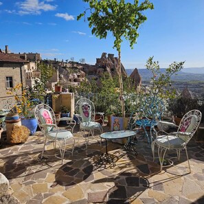 A patio with stone flooring and metal chairs, overlooking a mountainous landscape with traditional buildings. - Dancing Cloud Art Pansion (Nevsehir)