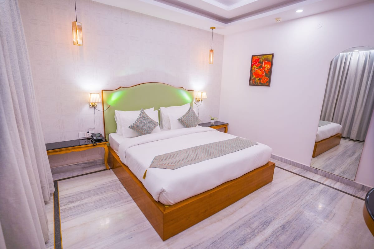 Habitación de hotel moderna con una cama grande, mesitas de noche, un espejo y un cuadro en la pared.