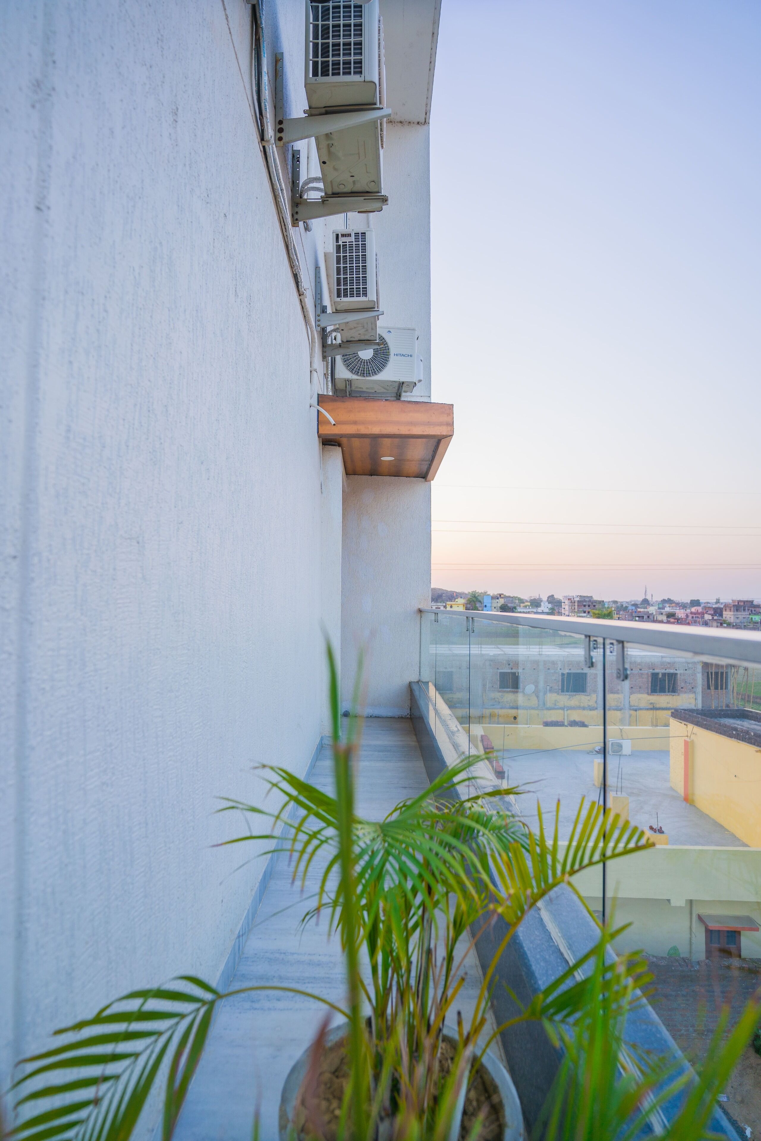 A balcony with a potted plant, air conditioning units, and a view of the cityscape.
