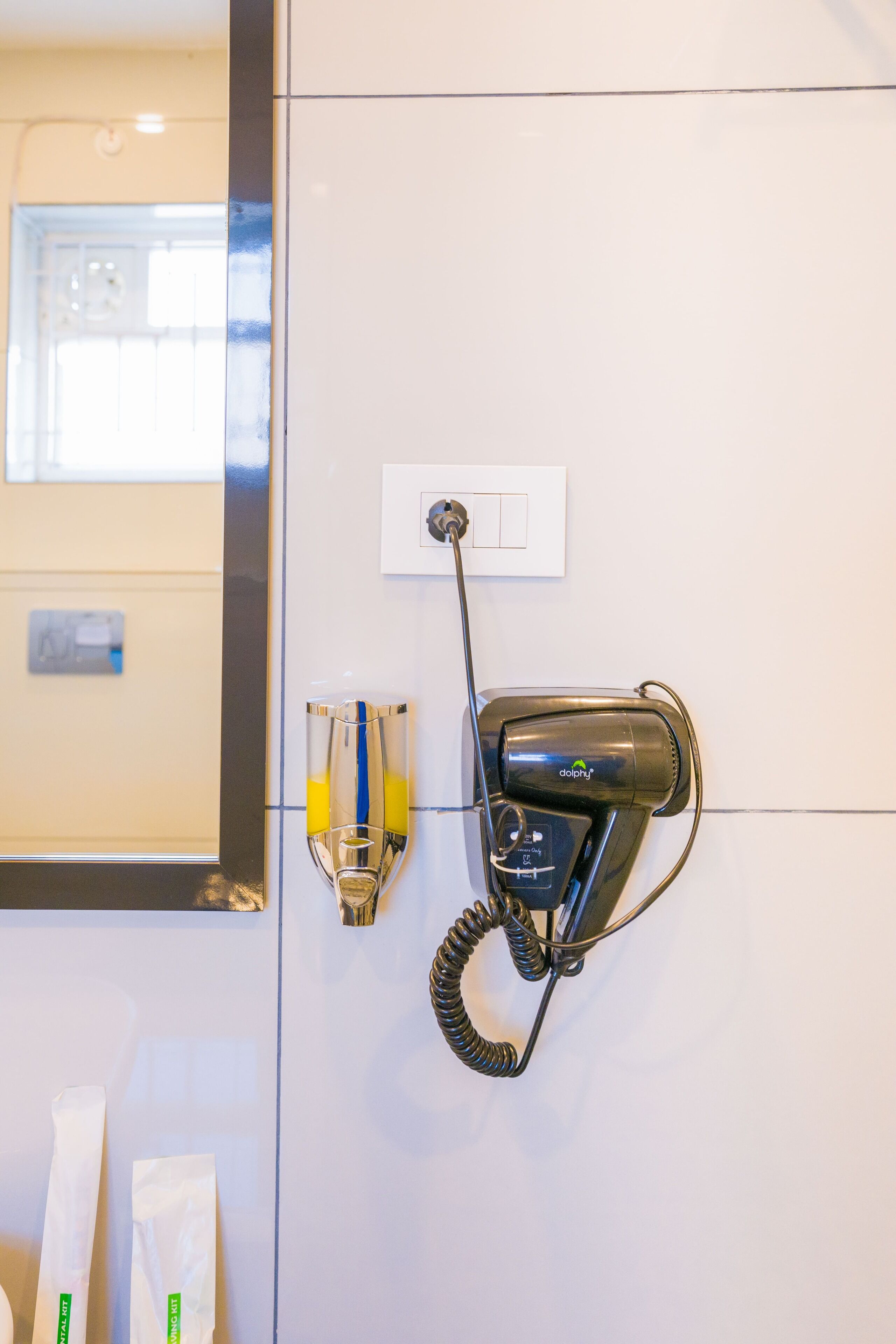 Un sèche-cheveux fixé au mur, une prise de courant et un miroir qui reflète une porte.