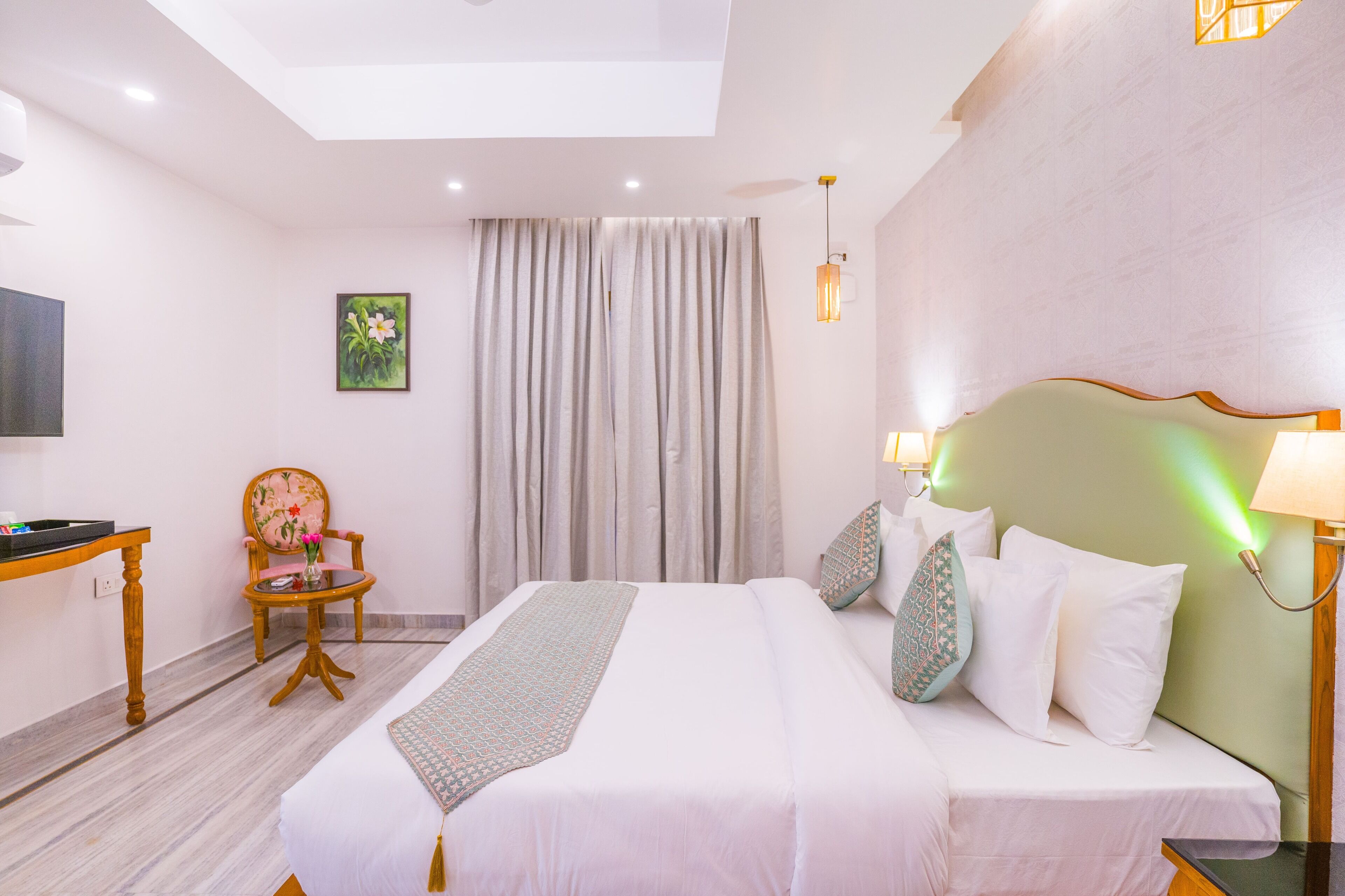 A hotel room with a large bed, a desk, a chair, and a painting on the wall.