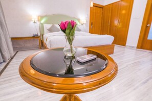 Une chambre d’hôtel avec un lit, une table de chevet ornée d’un vase de fleurs, une télécommande et une armoire en bois.