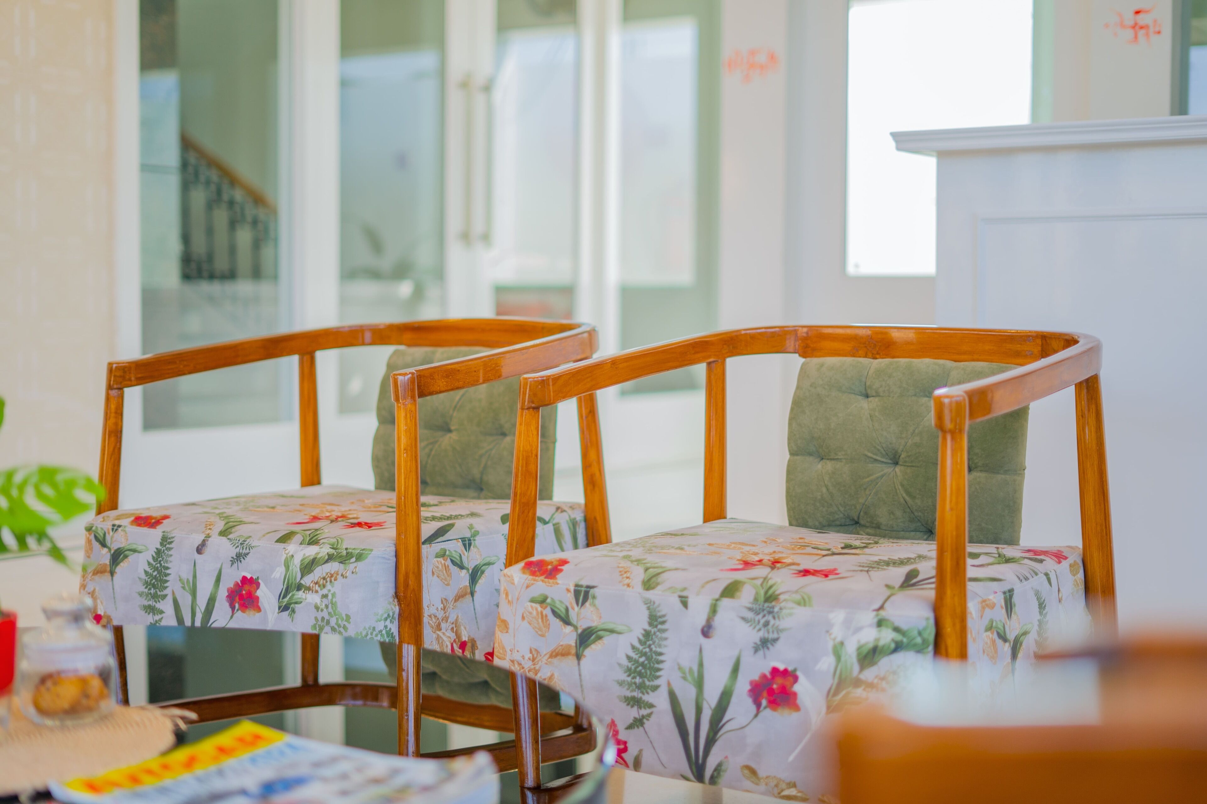 Two wooden chairs with floral upholstery, a glass table, and a white cabinet in a well-lit room.