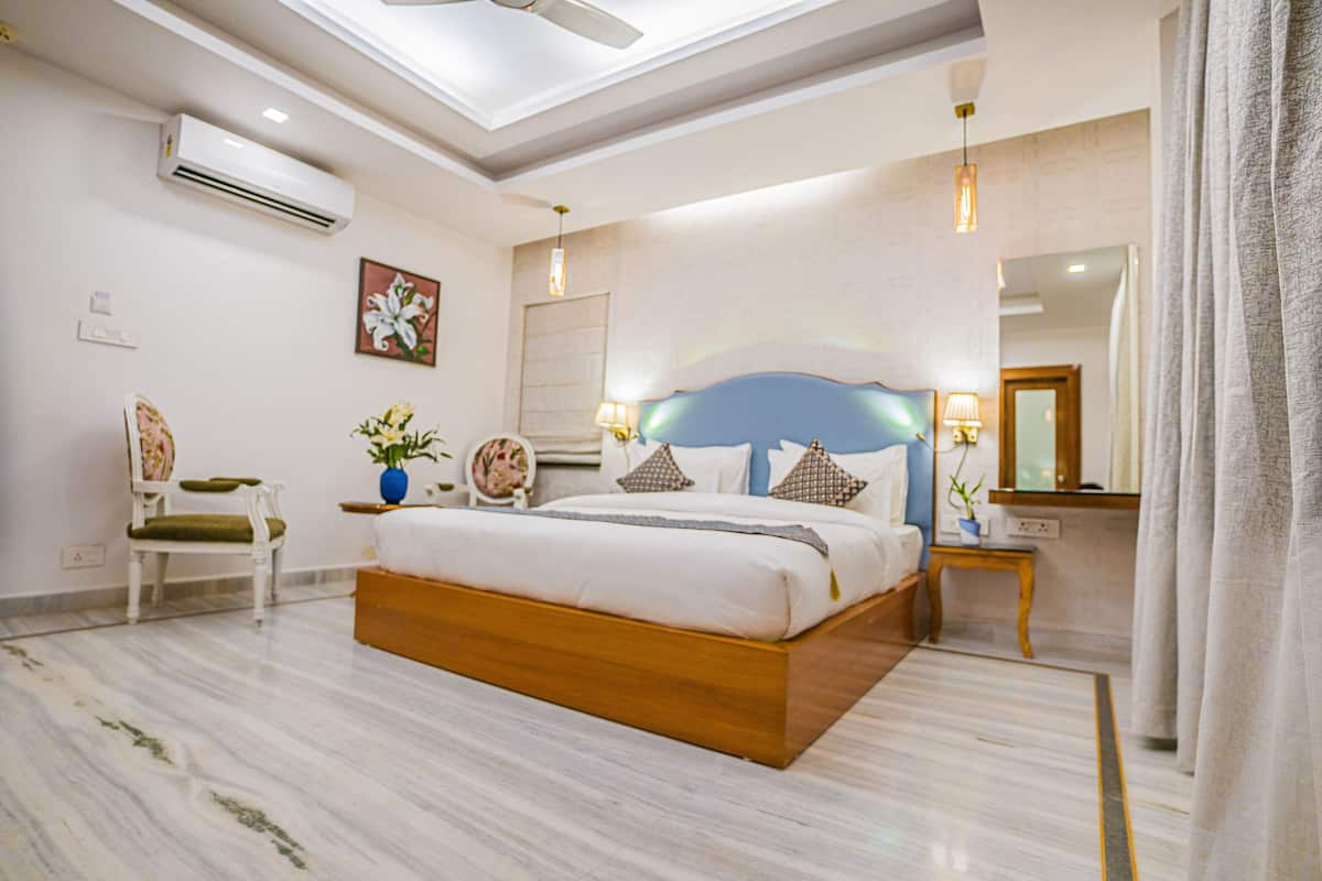 Un dormitorio amplio con una cama grande, ventilador de techo, aire acondicionado, mesita de noche con lámpara y espejo.
