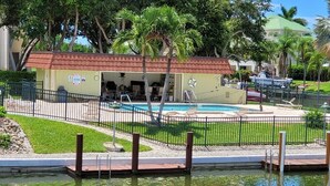 A pool area with a covered seating area, a lifeguard stand, and a small building with a red roof. - 2BR waterfront Marco Island condo with pool, WiFi, and heated pool. (Marco Island)
