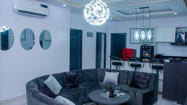 A modern living room with a grey sectional sofa, a round coffee table, and a unique chandelier. - Lawview Residential Services Apartment (Lekki)