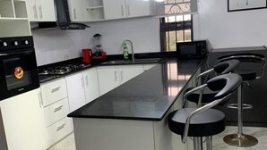 A modern kitchen with white cabinets, a black countertop, and a bar area with stools. - Lawview Residential Services Apartment (Lekki)
