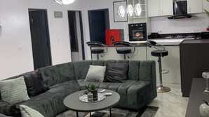A modern living room with a grey sectional sofa, a round coffee table, and a dining area with a dark table and chairs. - Lawview Residential Services Apartment (Lekki)