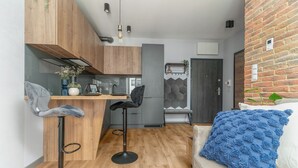 A compact living space with a kitchen, two bar stools, a sofa with a blue throw, and a brick wall. - MARGI Soho Apartament (Szczecin)