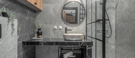 A modern bathroom with a marble sink, a round mirror, a wooden cabinet, and a glass shower enclosure.