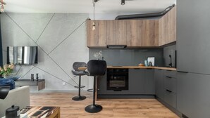 A modern kitchen with wooden cabinets, a built-in oven, and a bar stool. - MARGI Soho Apartament (Szczecin)