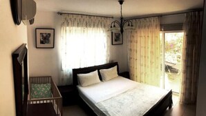 A bedroom with a large bed, a small crib, a ceiling fan, and a window with curtains. - 2 bedroom with private garden, walk to Nissi Beach
 (Ayia Napa)