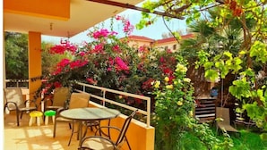 A patio with a round table and chairs, surrounded by vibrant bougainvillea flowers and lush greenery. - 2 bedroom with private garden, walk to Nissi Beach
 (Ayia Napa)