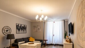 A living room with a sofa, a small table, a lamp, a TV, and artwork on the walls.