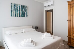 Una cama bien hecha con ropa y toallas blancas, un cuadro en la pared y un armario de madera.