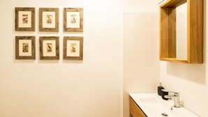A bathroom with a white sink, a wooden-framed mirror, and six framed pictures on the wall.