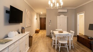 A modern kitchen with a dining area, white cabinetry, a flat-screen TV, and a chandelier.
