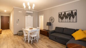 A living room with a dining table, chairs, a sofa, a lamp, and a wall clock.