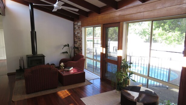 A spacious living room with a fireplace, large windows, and a view of a swimming pool. - Beautiful house, located in a quiet area of town with its own private pool (South West Rocks)