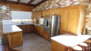 A kitchen with wooden cabinets, a stainless steel refrigerator, and a window. - Beautiful house, located in a quiet area of town with its own private pool (South West Rocks)