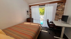A bedroom with a bed, a desk with a computer, a chair, and a view of a swimming pool through sheer curtains. - Beautiful house, located in a quiet area of town with its own private pool (South West Rocks)