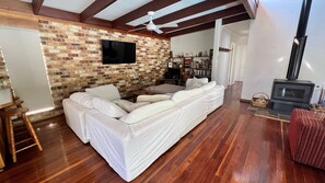 A living room with a brick wall, a flat-screen TV, a sofa, a wooden floor, and a fireplace.