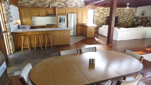 A kitchen with wooden cabinets, a stainless steel refrigerator, and a dining area with a round table and chairs. - Beautiful house, located in a quiet area of town with its own private pool (South West Rocks)