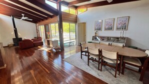 A spacious room with a wooden floor, a dining area with a table and chairs, a fireplace, and a large window providing natural light. - Beautiful house, located in a quiet area of town with its own private pool (South West Rocks)